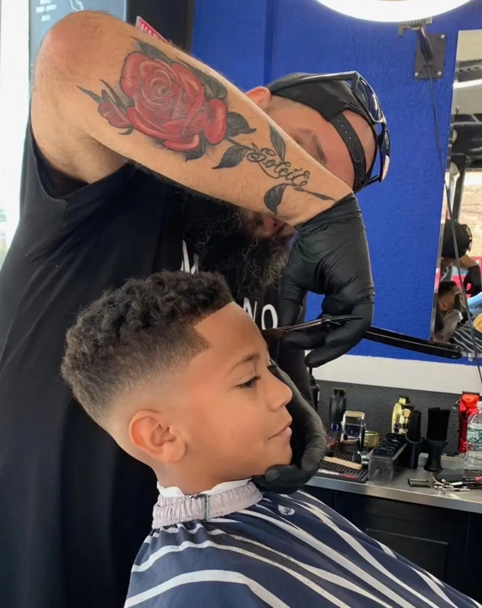 A tattooed Hair Wizards barber finishing a fade on a young boy